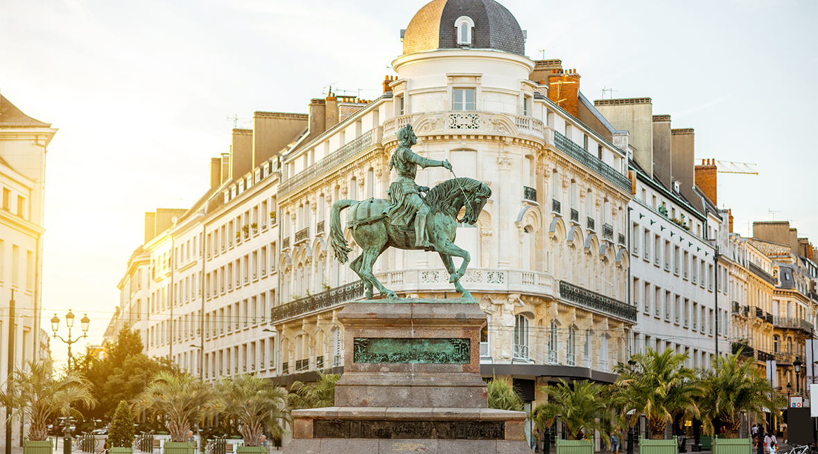 Equestrian statue, green from weathering, on a plinth in front of elegant period buildings at sunset or dawn